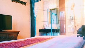 A bedroom with a bed, a dresser, a television, and a bathroom visible through a glass door. - Lijiang Shanju Zuihuayin Inn (Lijiang)
