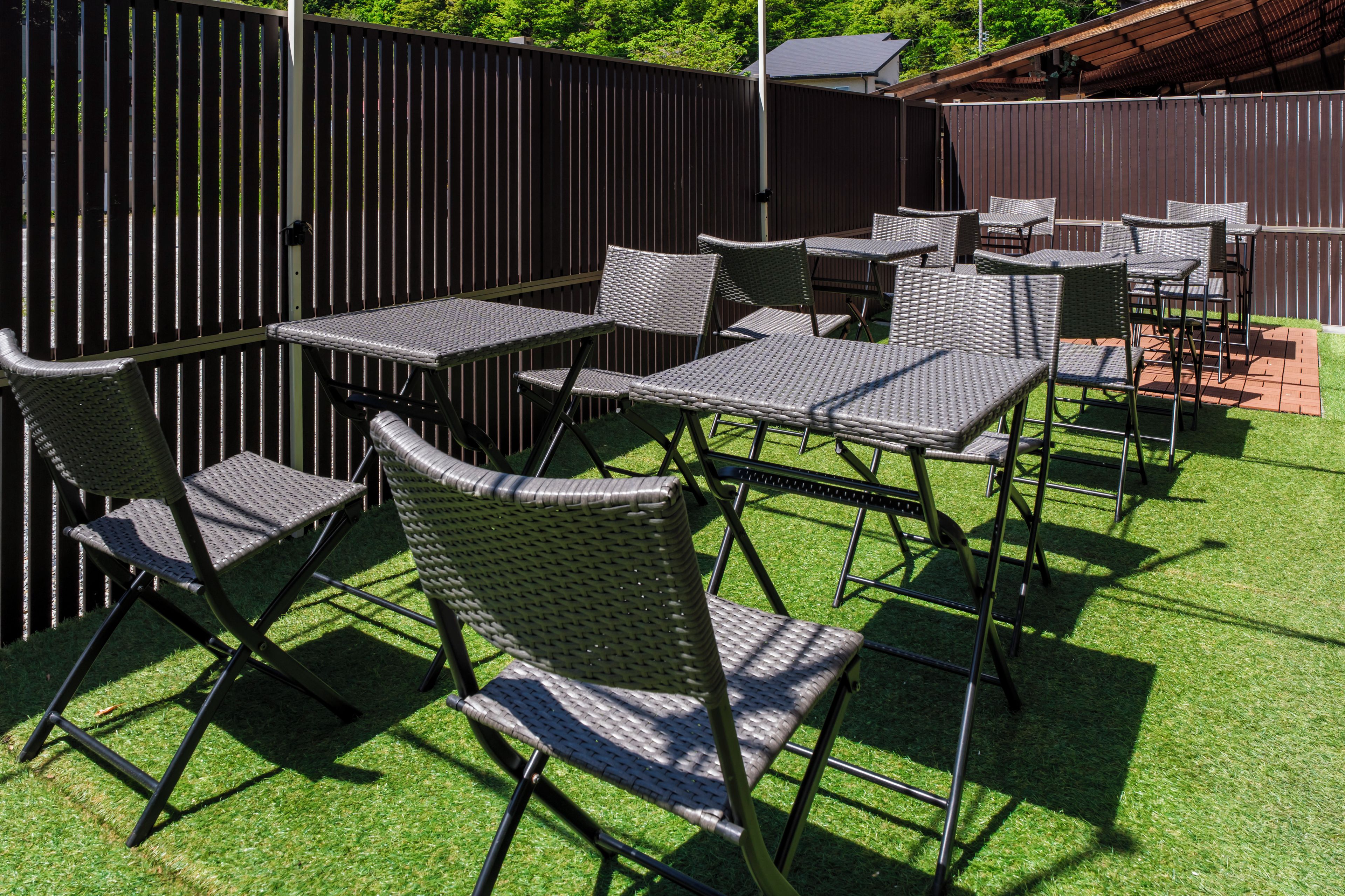An outdoor patio with multiple tables and chairs, surrounded by a wooden fence.
