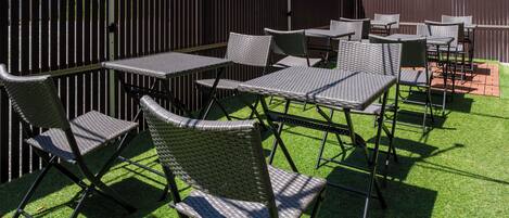 An outdoor patio with multiple tables and chairs, surrounded by a wooden fence.