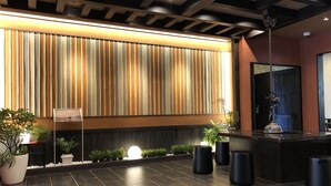A reception area with a modern design, featuring a large vertical panel with a striped pattern, a reception desk, potted plants, and a tiled floor. - Tabino Hotel Hida - Takayama (Takayama)