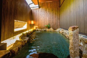 Un baño de aguas termales con paredes de madera, borde de piedra y una pequeña planta.