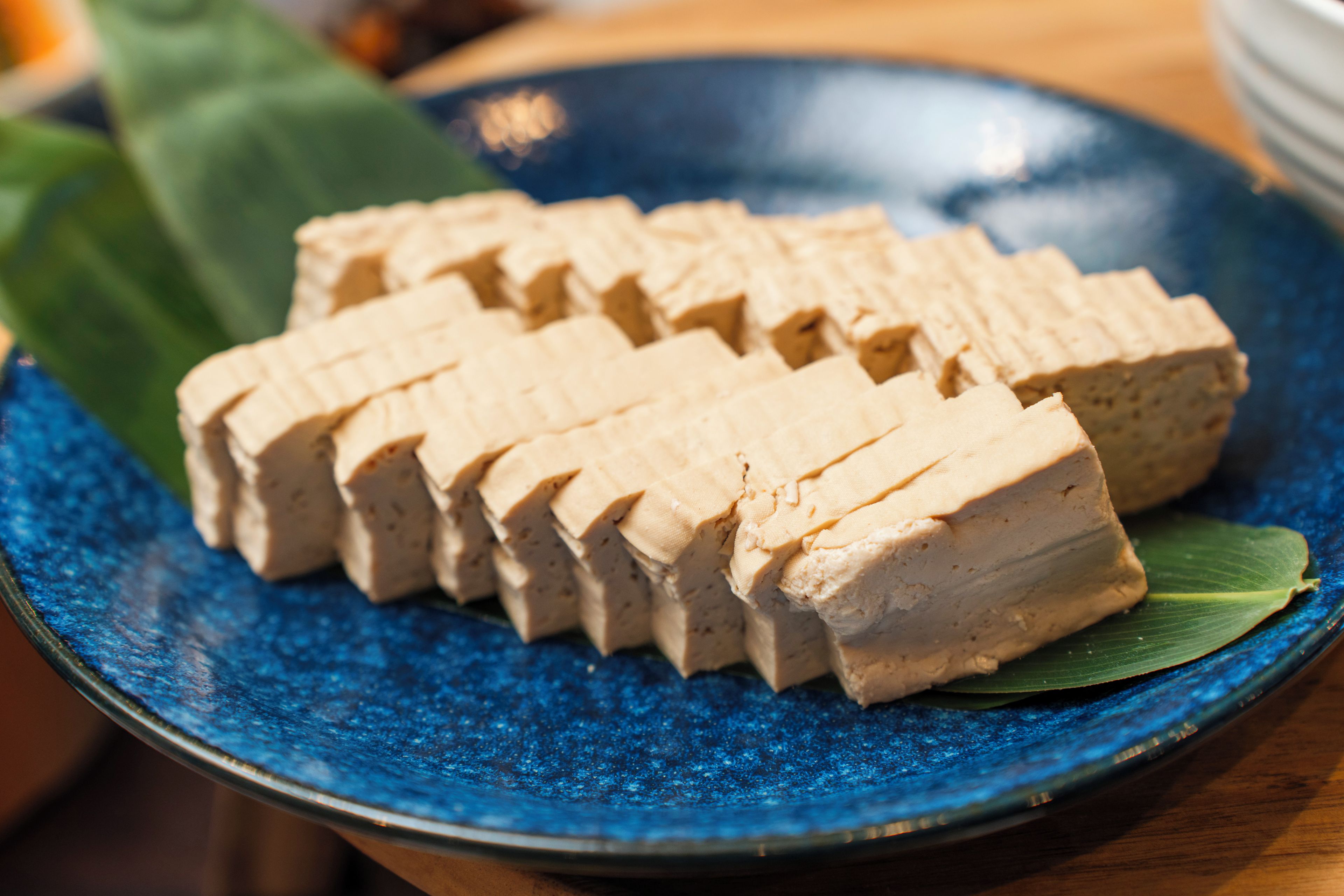A blue plate with tofu slices on a green leaf.