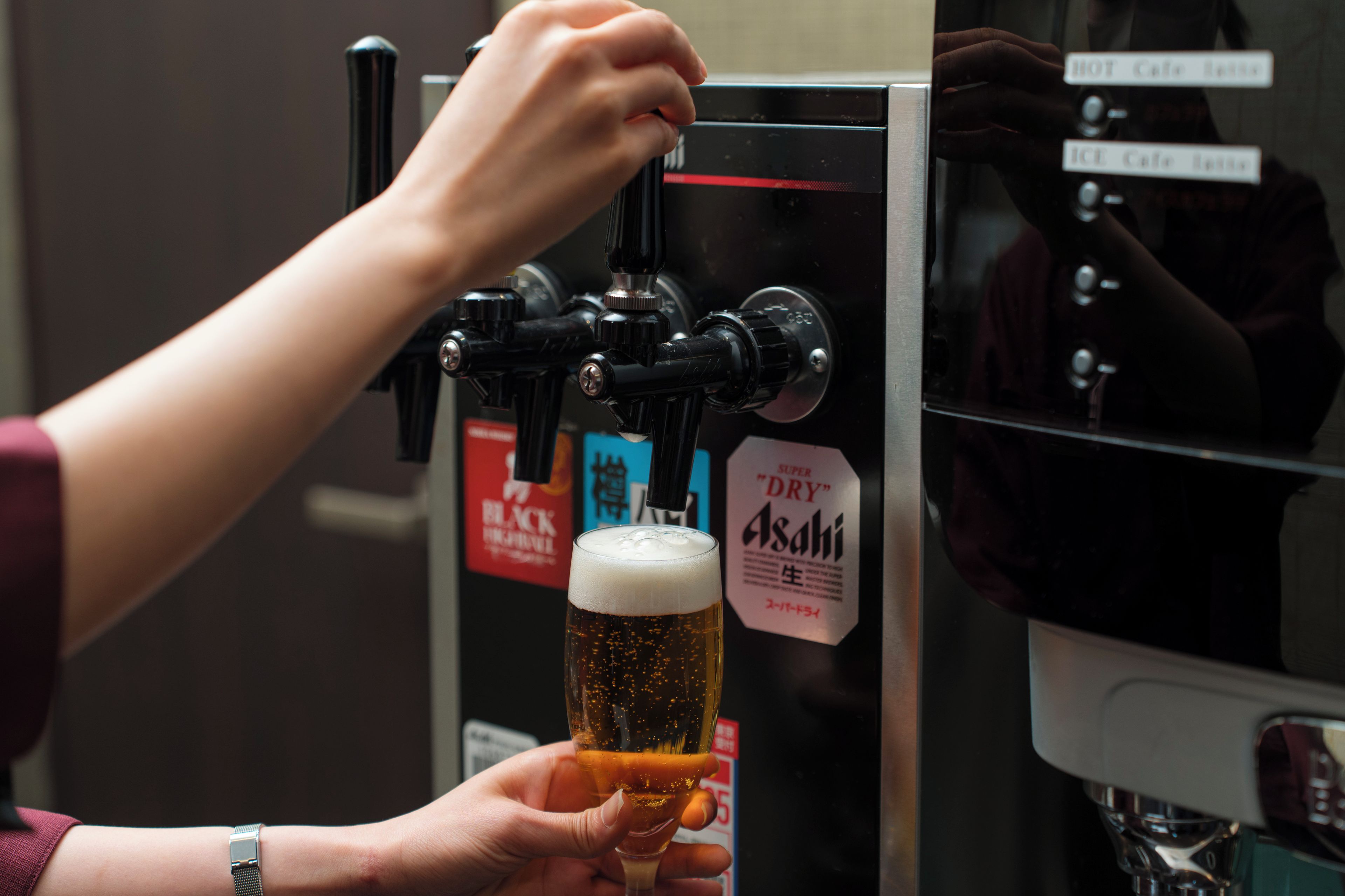 Una mano sostiene un vaso de cerveza debajo de un grifo, con etiquetas que indican opciones 'CALIENTE' y 'HELADO'.