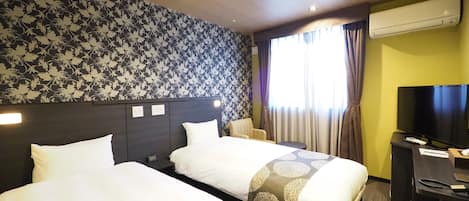 Quarto de hotel com duas camas, televisão de tela plana, escrivaninha e janela com cortinas.