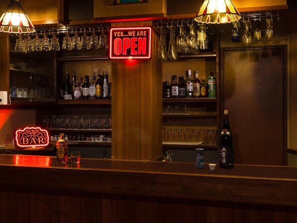 A bar area with a neon sign indicating it is open, shelves stocked with bottles, and a variety of glasses. - Petit Hotel P-Bow (Hakuba)