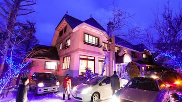 A large, multi-story house with a prominent front entrance, surrounded by snow and decorated with blue lights.