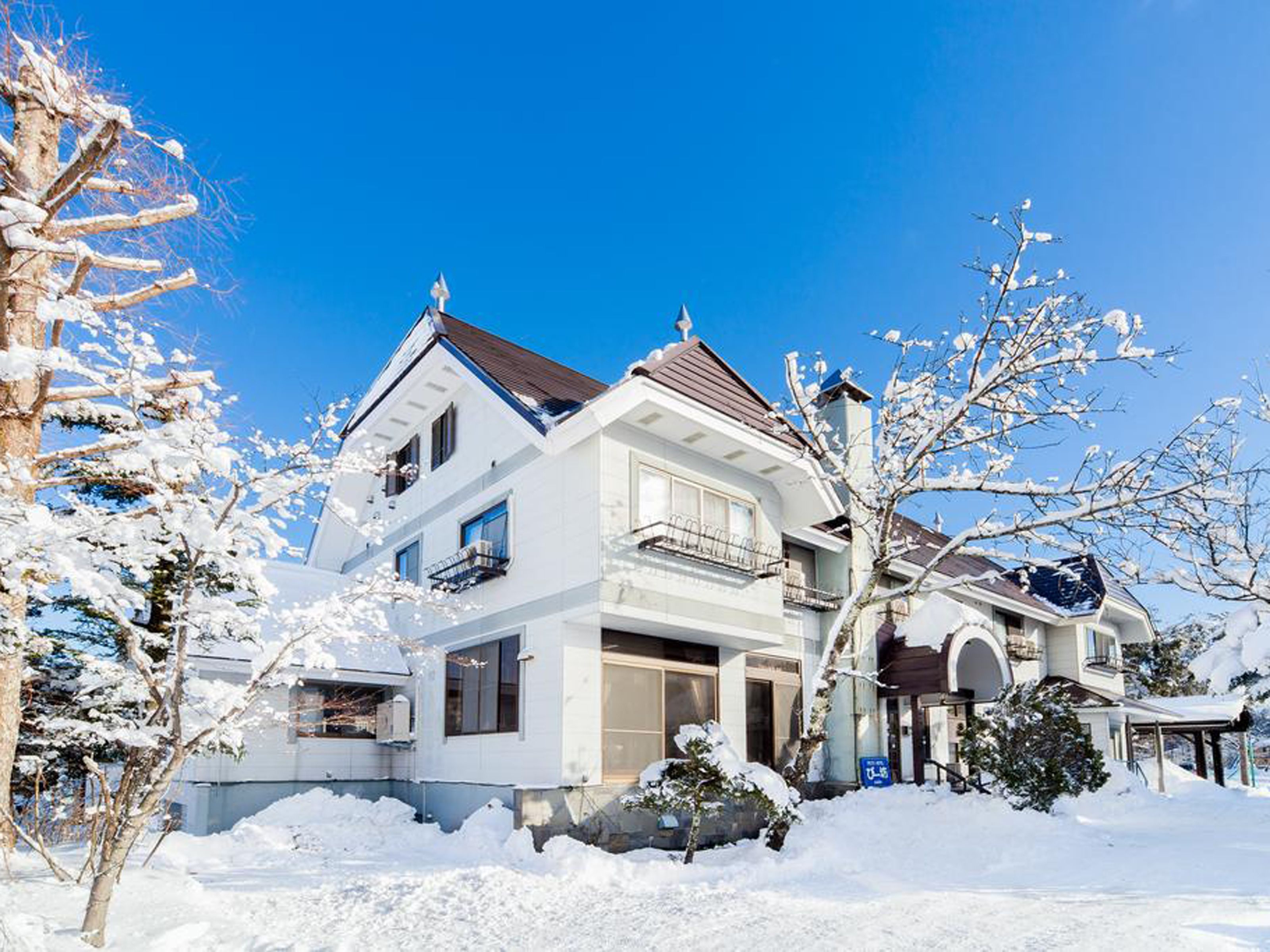 A two-story house with a white exterior, a brown roof, and a balcony on the second floor.