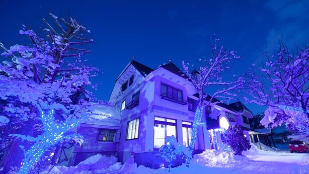 A two-story house with a snow-covered driveway and trees. - Petit Hotel P-Bow (Hakuba)