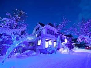 A two-story house with a snow-covered driveway and trees. - Petit Hotel P-Bow (Hakuba)