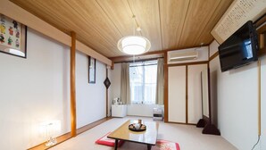 A traditional Japanese-style room with tatami flooring, a low table with a tray, a television mounted on the wall, and a sliding door. - Petit Hotel P-Bow (Hakuba)