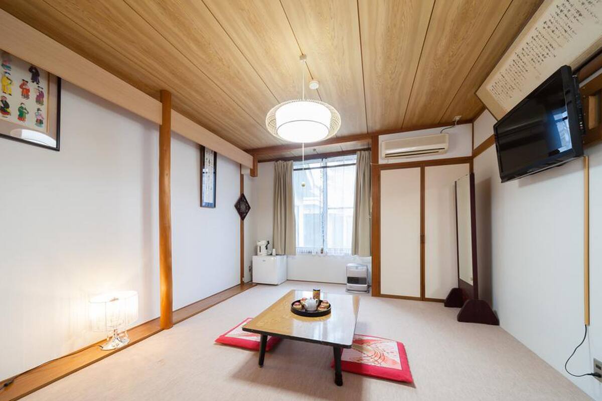 A traditional Japanese-style room with tatami flooring, a low table with a tray, a television mounted on the wall, and a sliding door.