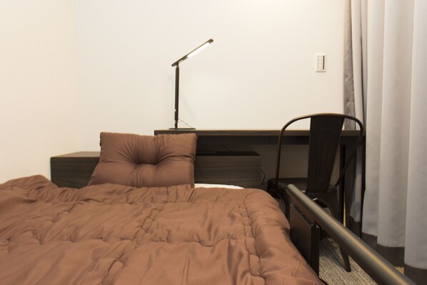 A neatly made bed with a brown comforter, a bedside lamp, a chair, and a small table with a lamp. - Ryoma Ikebukuro I - Hostel (Tokyo)