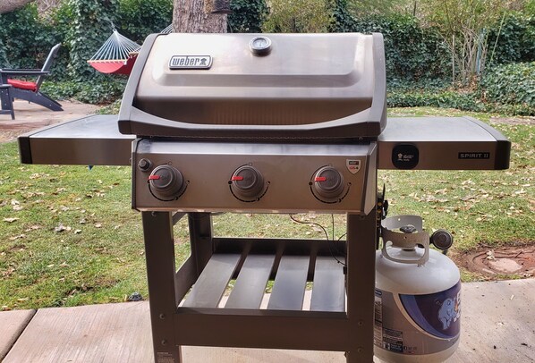 A Weber Spirit II grill with a gas tank, control knobs, and a built-in thermometer.