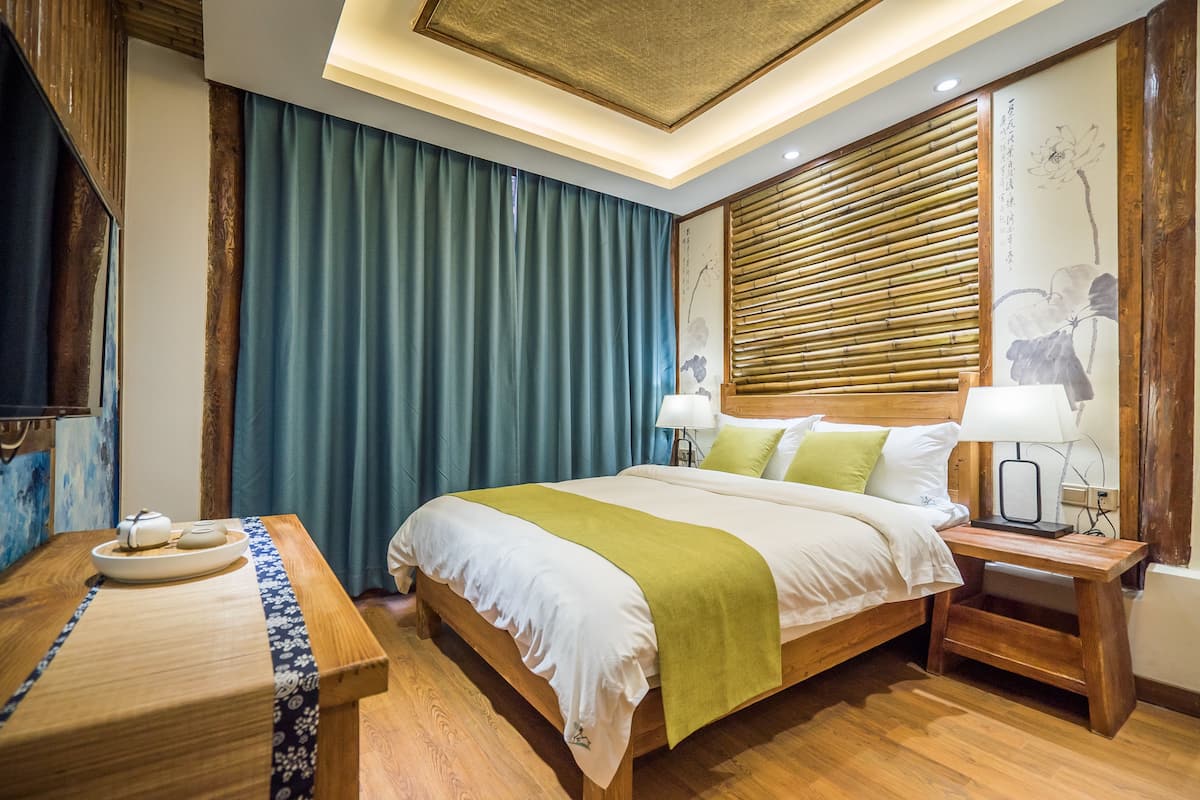 A neatly arranged hotel room with a large bed, bedside tables, a wooden desk, and a traditional-style wall with a curtain.