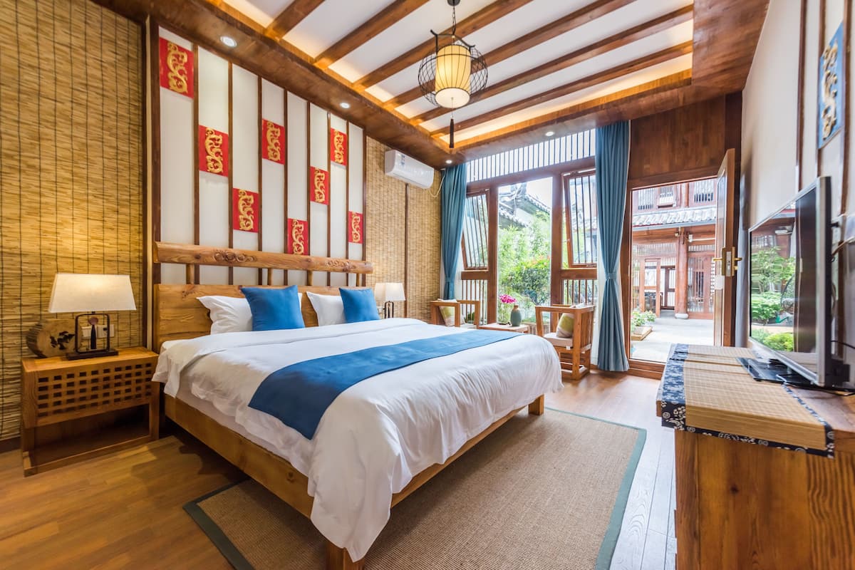A spacious bedroom with a large bed, wooden headboard, and a view of the garden through the open door.