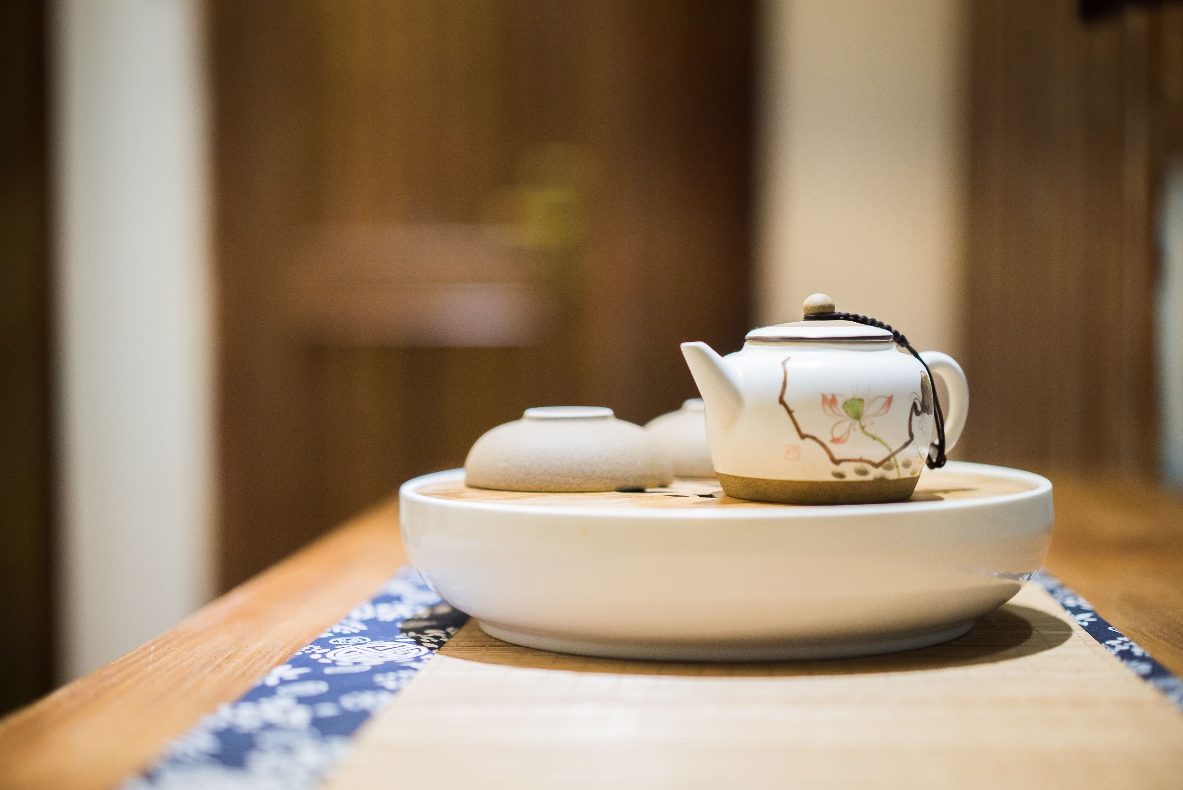 Una teiera e una tazza su un piatto bianco su un tavolo di legno con una tovaglia a motivi blu.