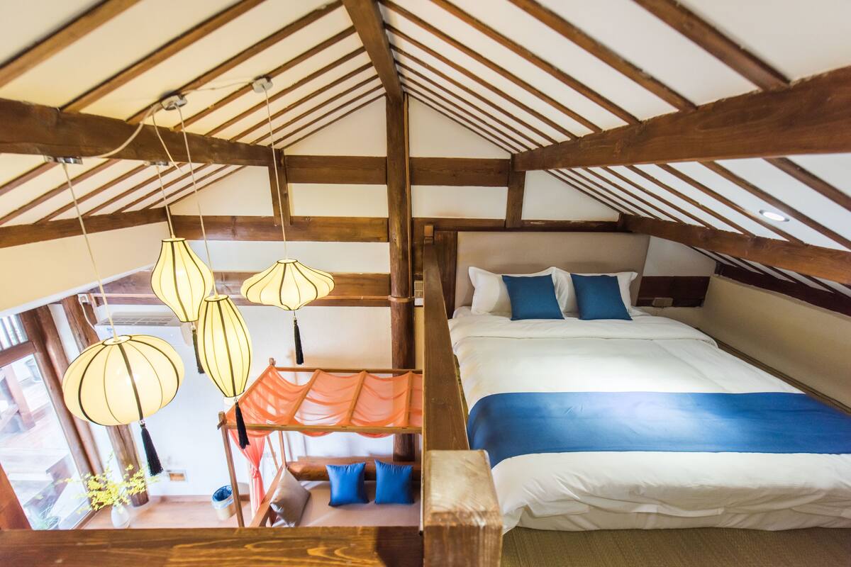 A bedroom with a wooden ceiling, a bed with blue bedding, and hanging lamps.