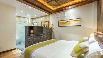 A modern hotel room with a large bed, a flat-screen TV, a stone accent wall, and a ceiling with wooden beams.