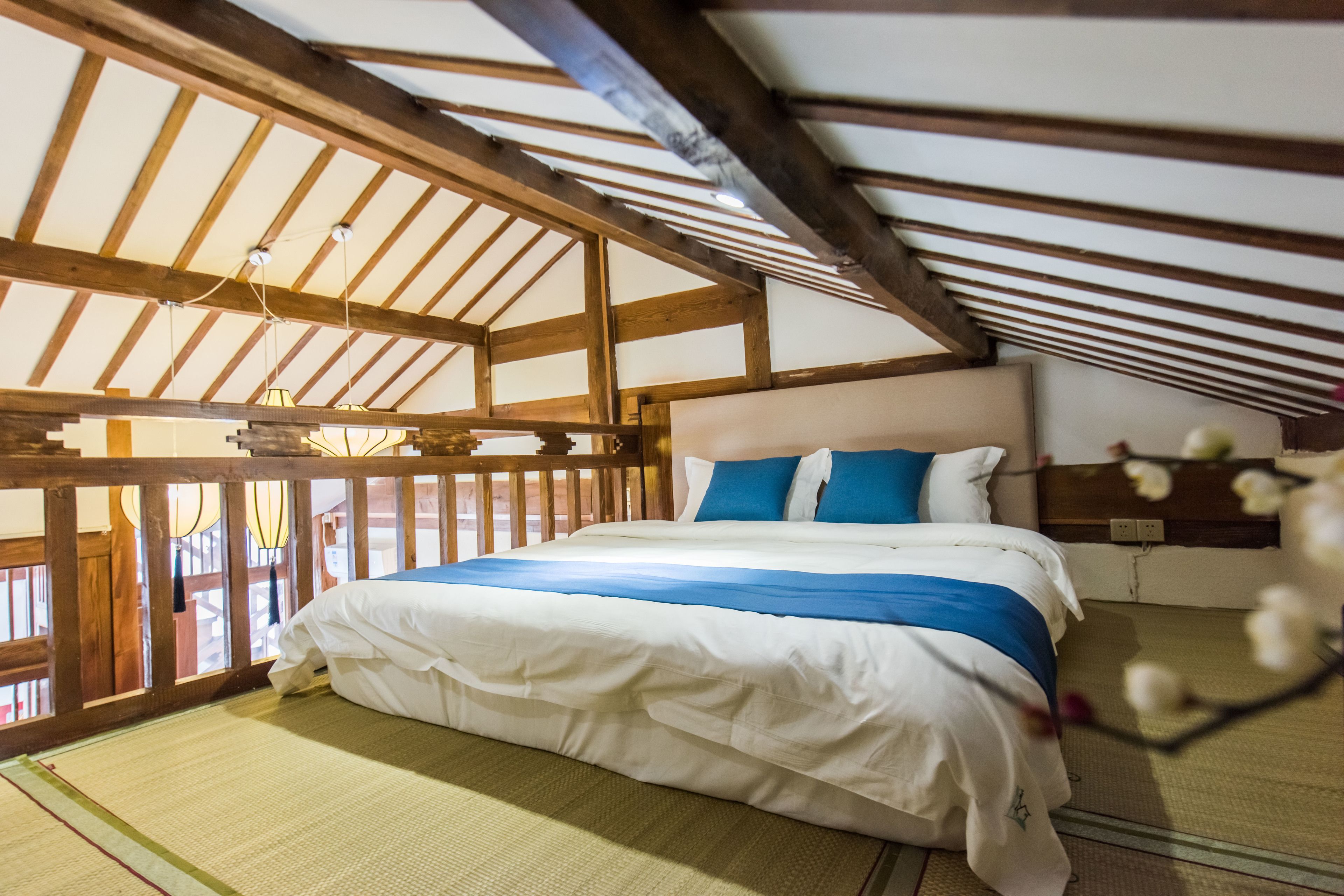 Une pièce avec un lit, des poutres en bois, un revêtement de sol en tatami et un luminaire suspendu.