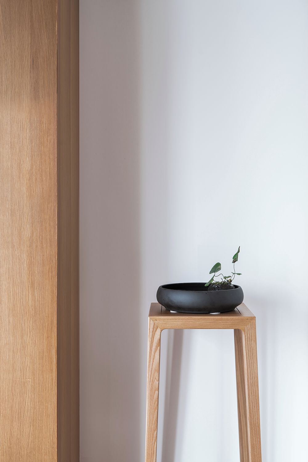 A wooden stool with a black bowl containing a small plant.