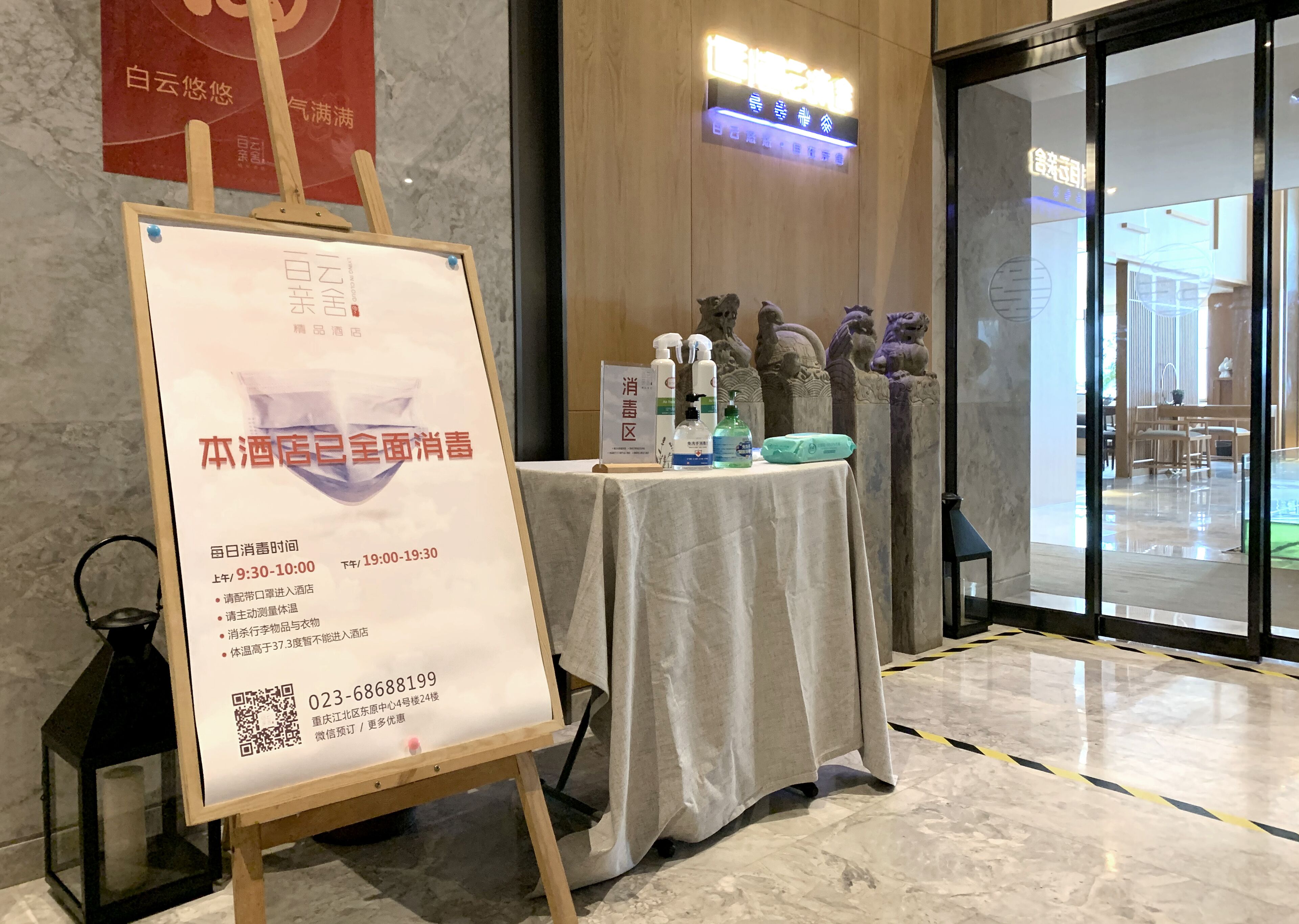 Un hall de hotel con un cartel que detalla las precauciones por COVID-19, una mesa con dispensadores de desinfectante para manos y estatuas decorativas.