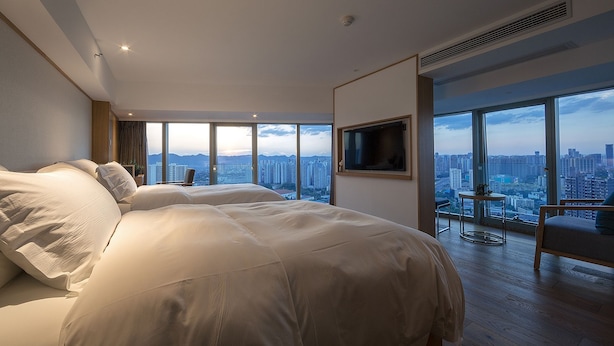 A spacious bedroom with a large bed, a TV mounted on the wall, and a city view through large windows. - Chongqing White Cloud Boutique Hotel (Chongqing)