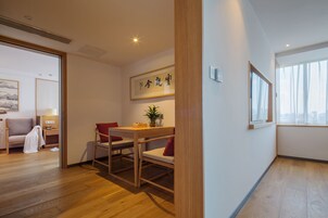 Una habitación de hotel moderna con piso de madera, una mesa de comedor con sillas, una pequeña planta en maceta y una obra de arte enmarcada en la pared.