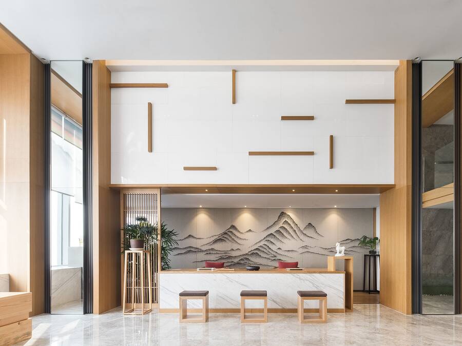 Un área de recepción moderna con un mostrador de madera, tres taburetes y una pared decorativa con un paisaje de montaña.