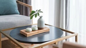 A round table with a wooden tray holding a vase and two small cups, set on a wooden floor with a sofa and curtains in the background. - Chongqing White Cloud Boutique Hotel (Chongqing)
