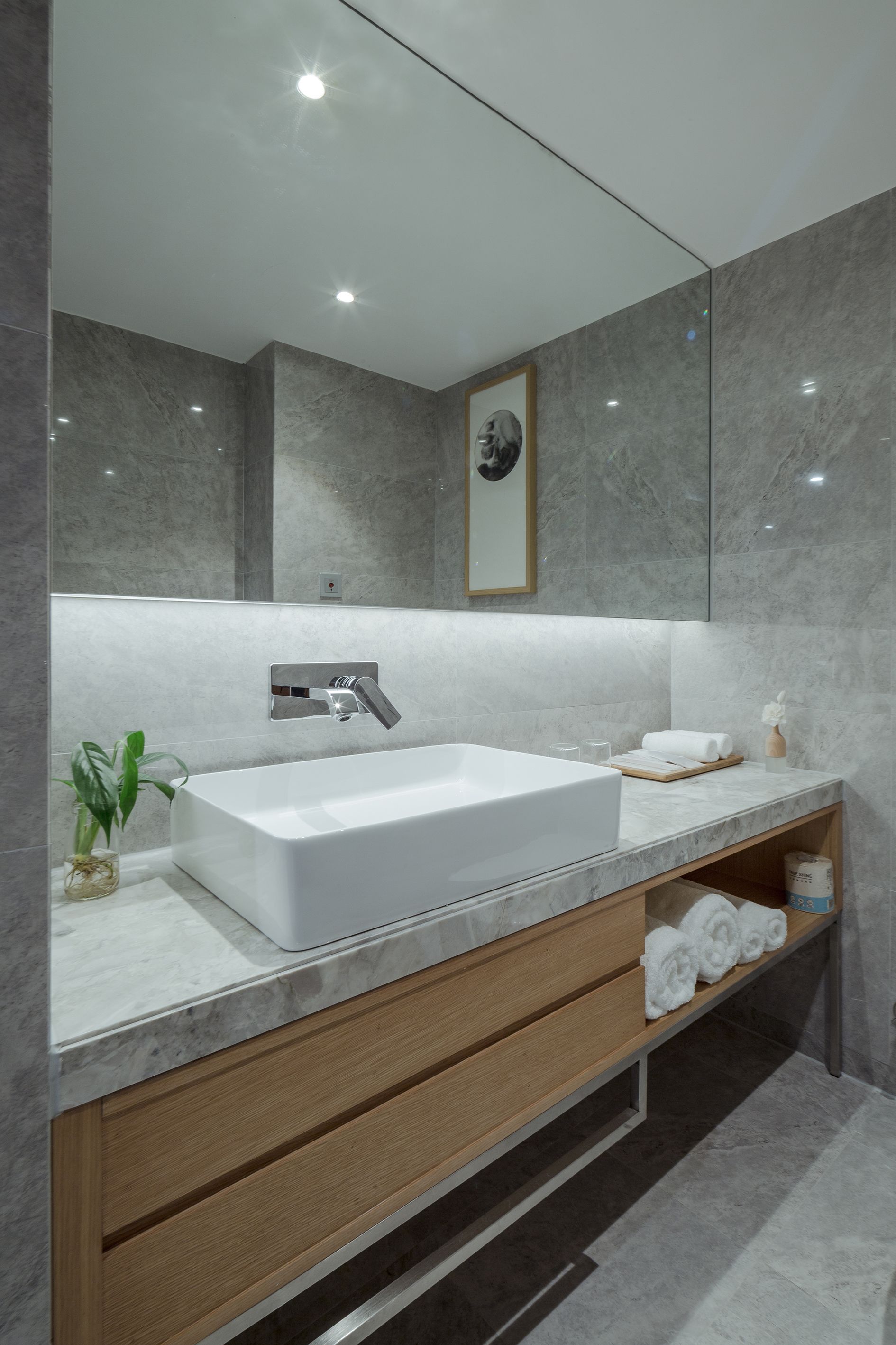 Une salle de bain moderne avec une grande baignoire blanche, un meuble-lavabo en bois, des murs en marbre et un tableau encadré au-dessus du miroir.