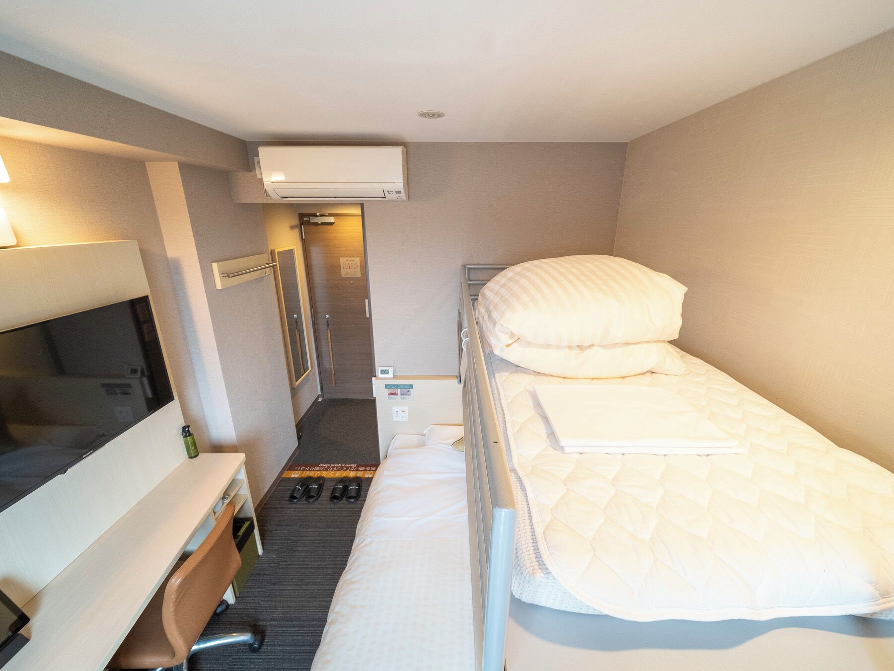 A small, clean room with a bed, a desk, a chair, and a TV.