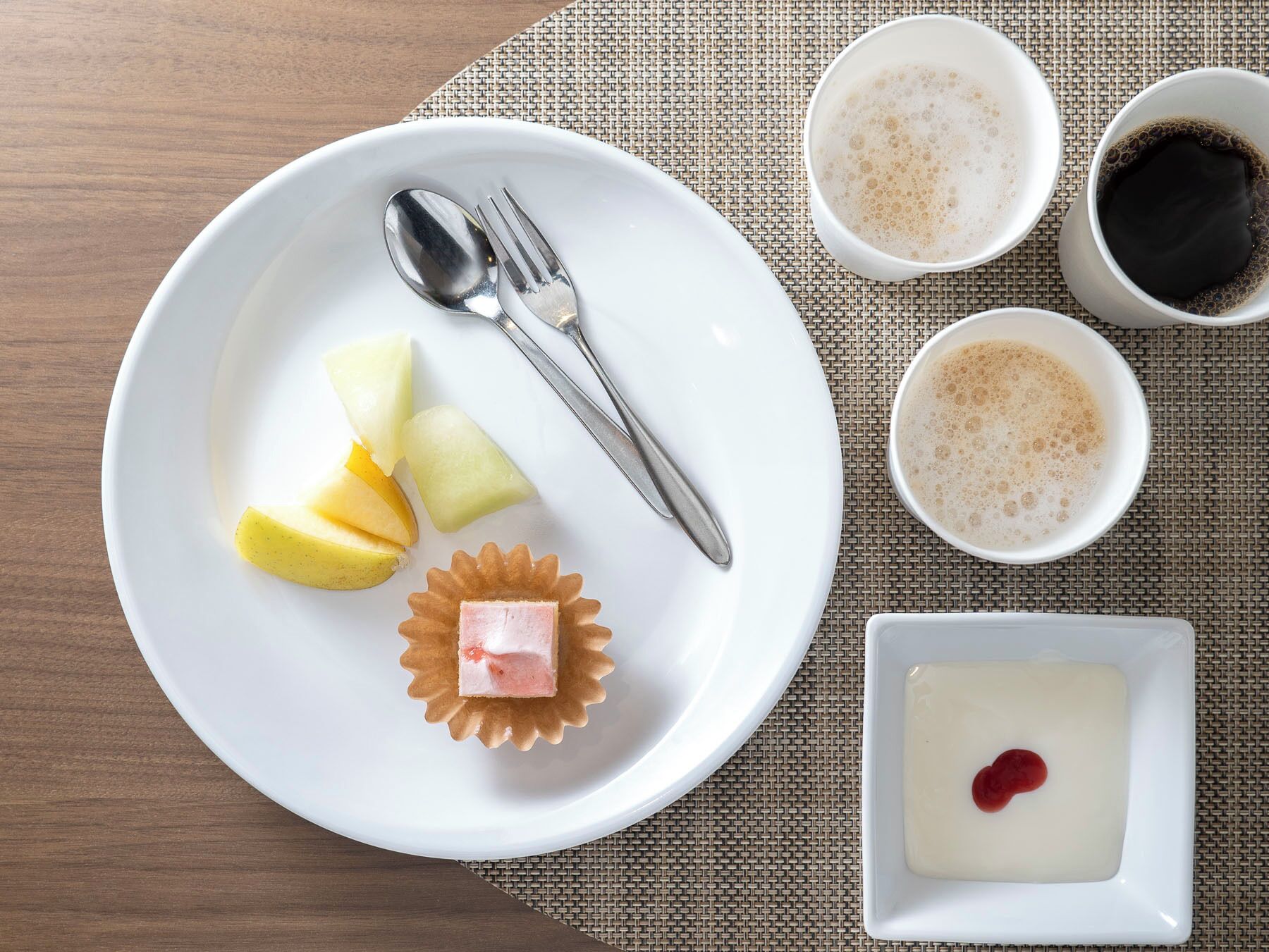 Un plato blanco con cuchara, tenedor y una pequeña tarta sobre un mantel individual.