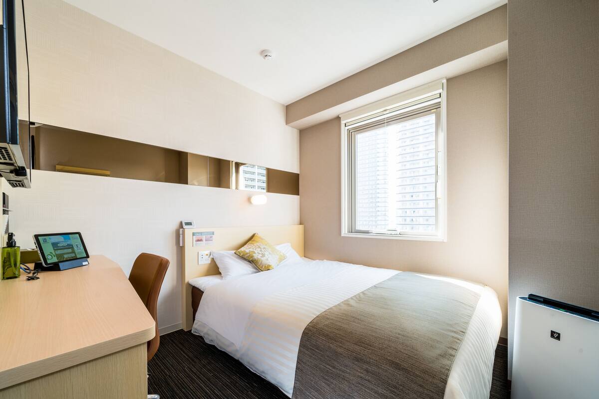 Una habitación de hotel con cama, escritorio, silla y un refrigerador pequeño.