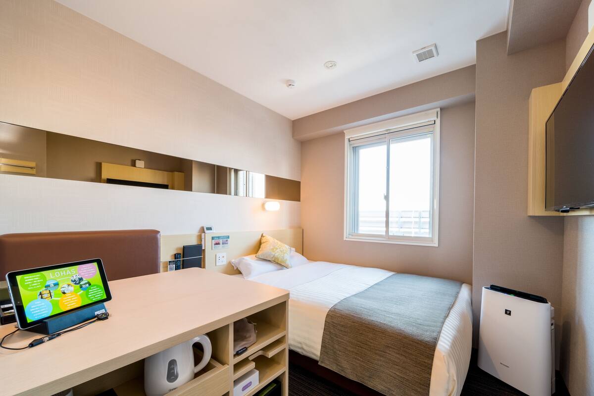Habitación de hotel con cama, escritorio con una tablet, cafetera, televisor y mini refrigerador.