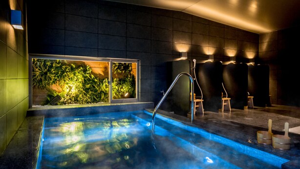 Piscina interior moderna com parede de vidro transparente, vapor subindo da água e interior escuro com iluminação ambiente.