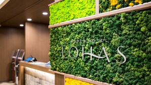 Uma área de recepção com parede coberta de musgo verde e amarelo, e o nome 'LOHAS' em destaque.