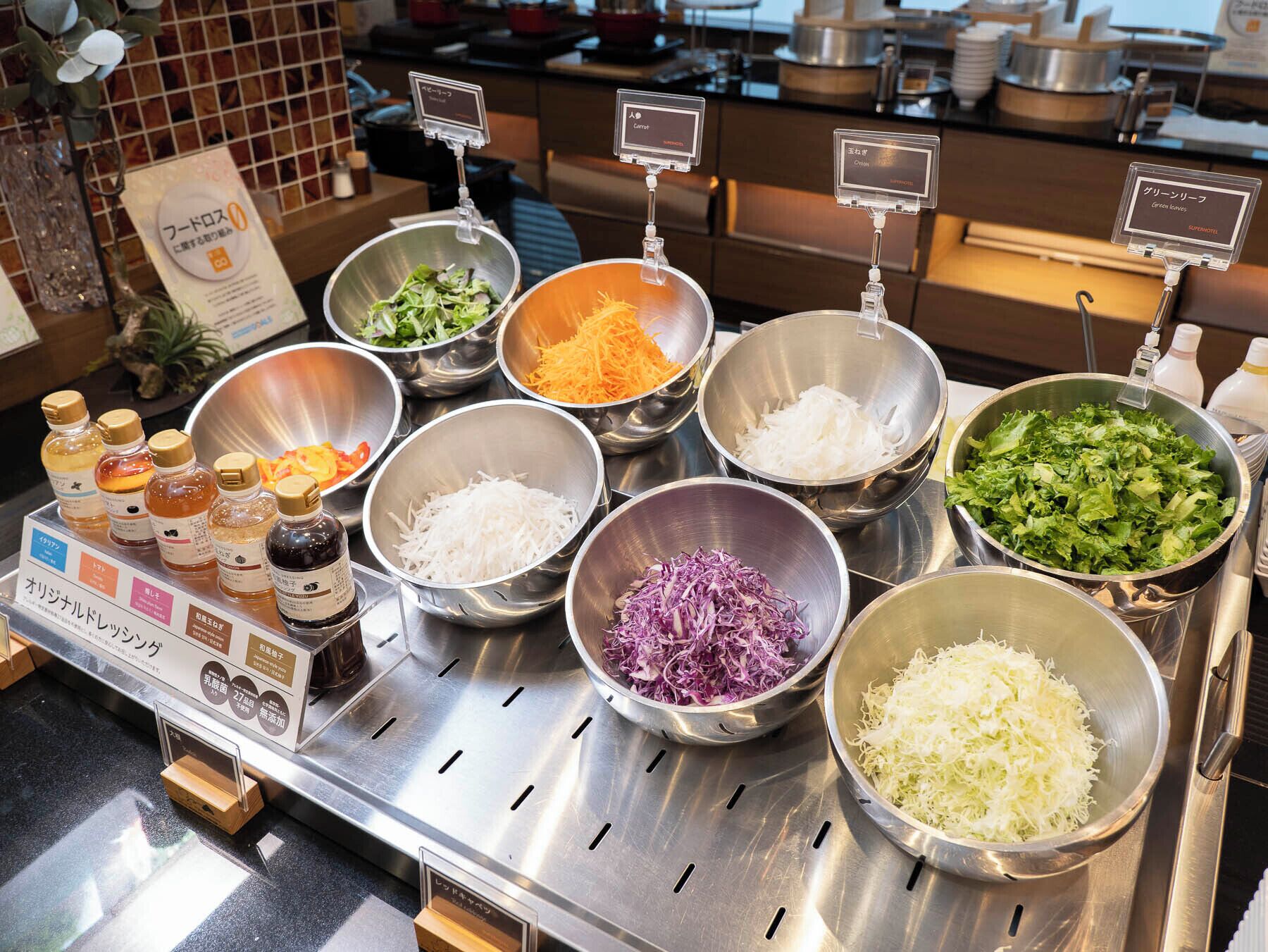 Un bufé con diversos alimentos en recipientes, incluyendo verduras ralladas y ensaladas.