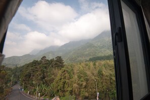 A view from inside a vehicle, looking out at a winding road through a mountainous area with dense greenery and clouds in the sky. - Place of Heart (Lugu)