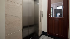 A modern elevator with a metallic finish, a wooden door, and a tiled floor. - Place of Heart (Lugu)