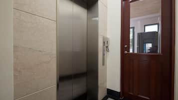 A modern elevator with a metallic finish, a wooden door, and a tiled floor.