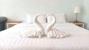 Quarto de hotel com cama, duas mesas de cabeceira, abajur e arranjo de toalhas em formato de cisne decorativo.