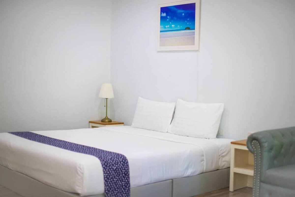 A neatly made bed with white linens and a blue patterned throw, a bedside lamp, and a framed picture on the wall.