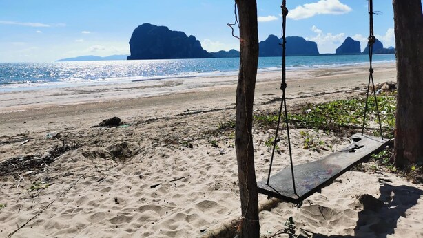 Uma praia com baloiço e vista para o mar e ilhas distantes.