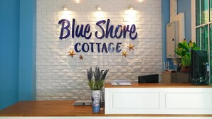 Uma mesa de recepção com uma parede de tijolos brancos ao fundo, exibindo o texto "Blue Shore Cottage" com estrelas decorativas.