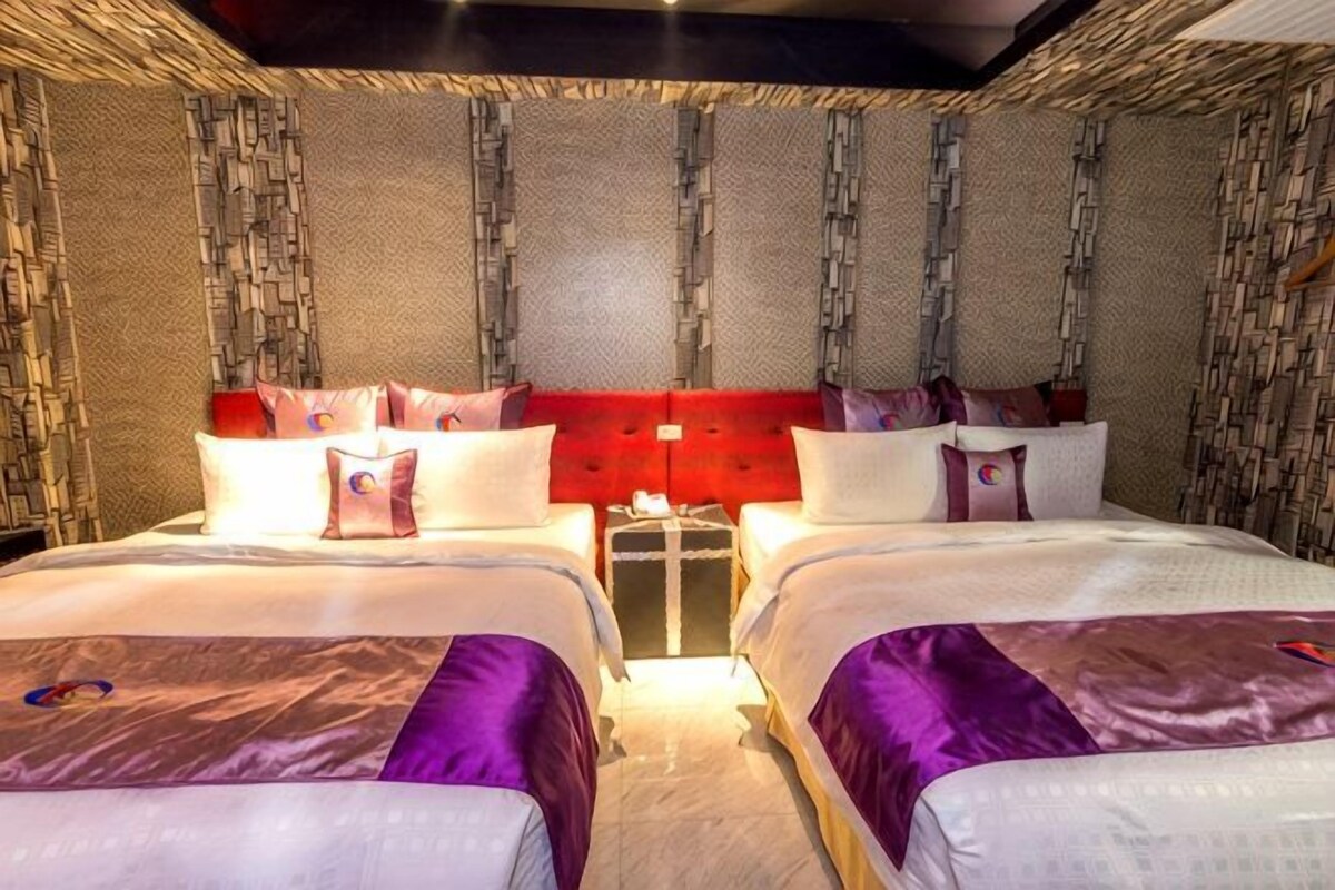 Habitación de hotel con dos camas, un cabecero rojo y una mesita entre ellas.