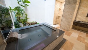 Een wellnessruimte met een jacuzzi, omringd door potplanten en een bakstenen muur.