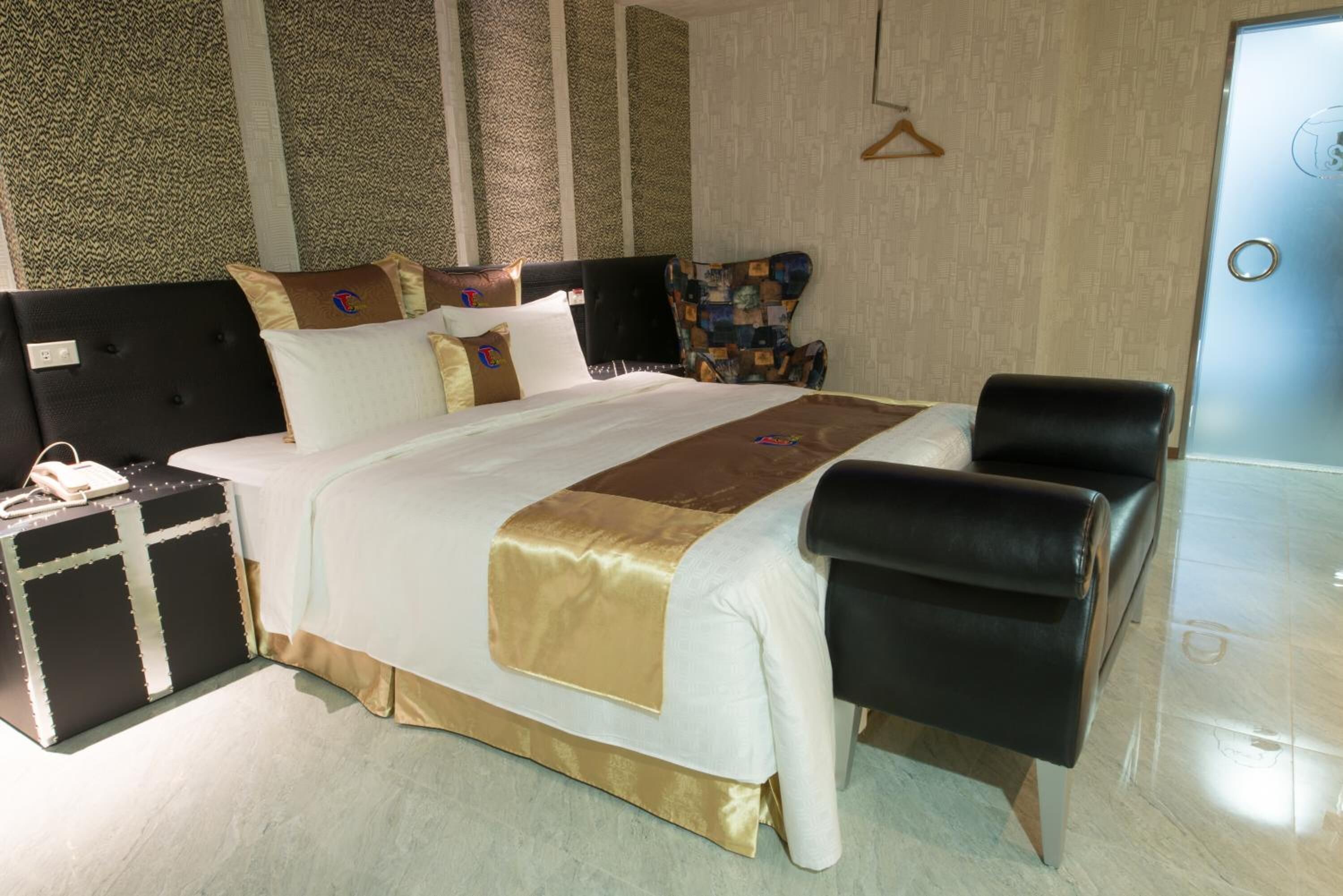 Una habitación de hotel con una cama grande, una mesita de noche, un sillón de cuero negro y un armario.