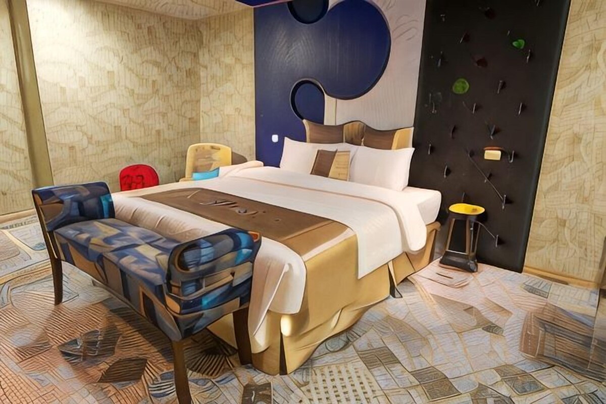 A modern hotel room with a large bed, a bench, a bedside table, and a wall with a unique design.