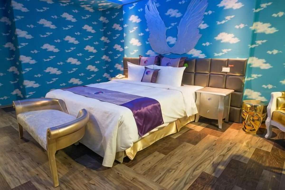 Een slaapkamer met een groot bed, een nachtkastje, een stoel en een muur met een wolkpatroon.