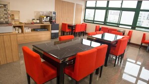 Een eetgedeelte met rode stoelen en een zwarte tafel, een koffieapparaat en een toonbank met etenswaren.